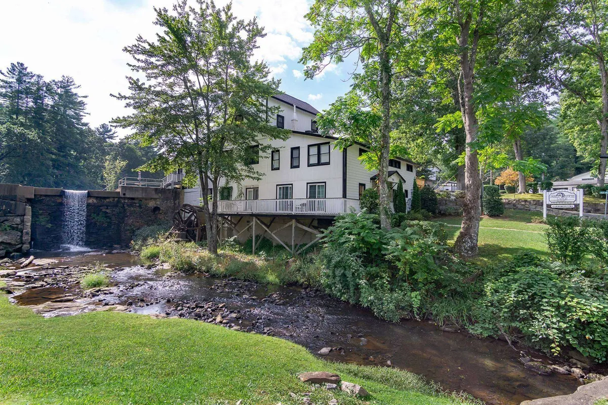 A picturesque waterfall framed by trees and a stream, with a building visible in the background. The area invites guests to relax, fish, picnic, or simply enjoy the soothing sounds and sights of cascading water.