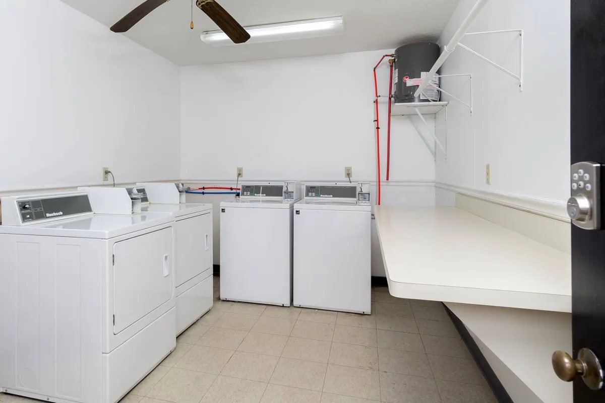 A bright and organized laundry room featuring washers, dryers, and a spacious folding table. The room is clean and practical, providing convenience for extended stays and efficient daily routines.
