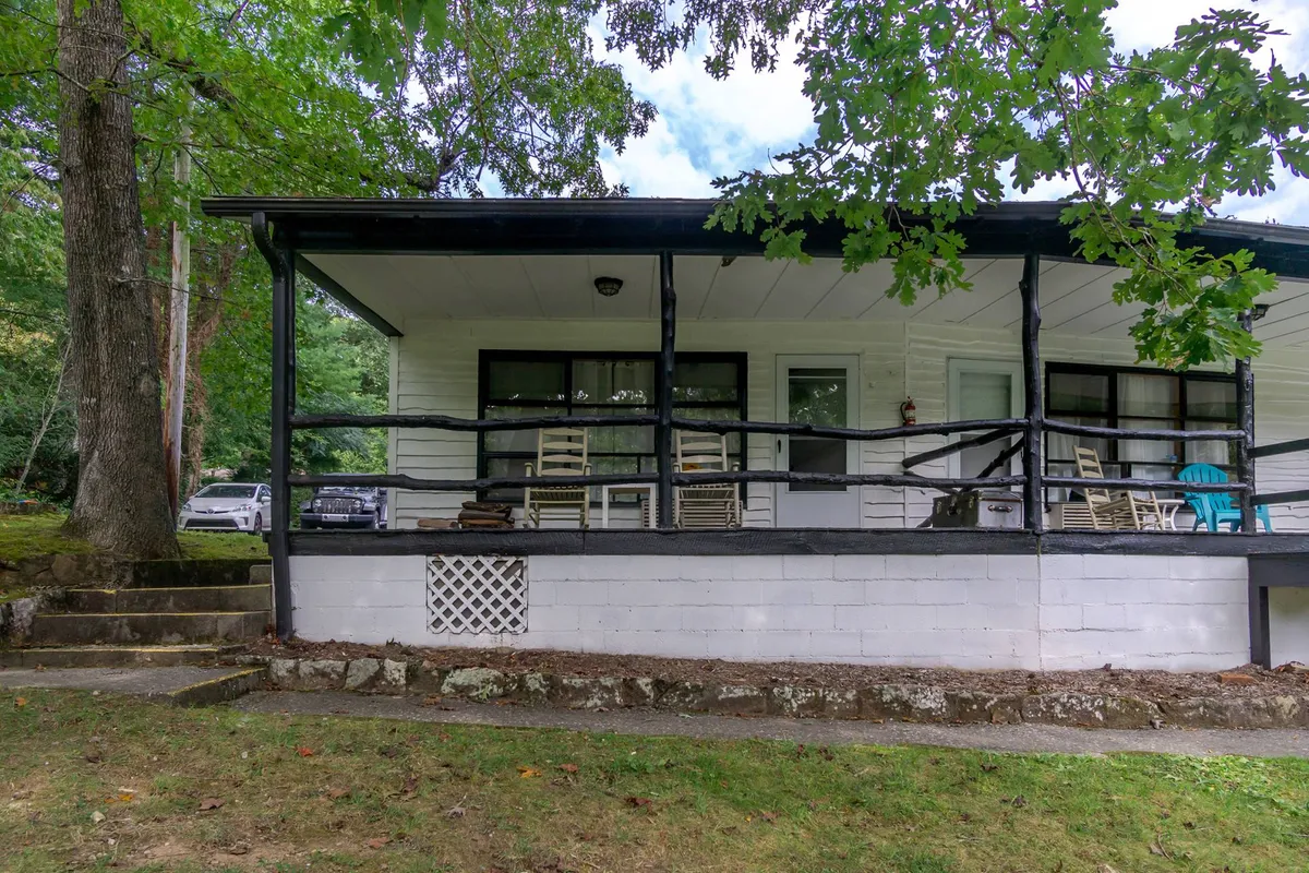 A welcoming porch with rocking chairs and a cheerful blue chair facing green trees, framing a peaceful spot for morning coffee, sunset watching, or socializing with loved ones. The setting conveys relaxation and togetherness.