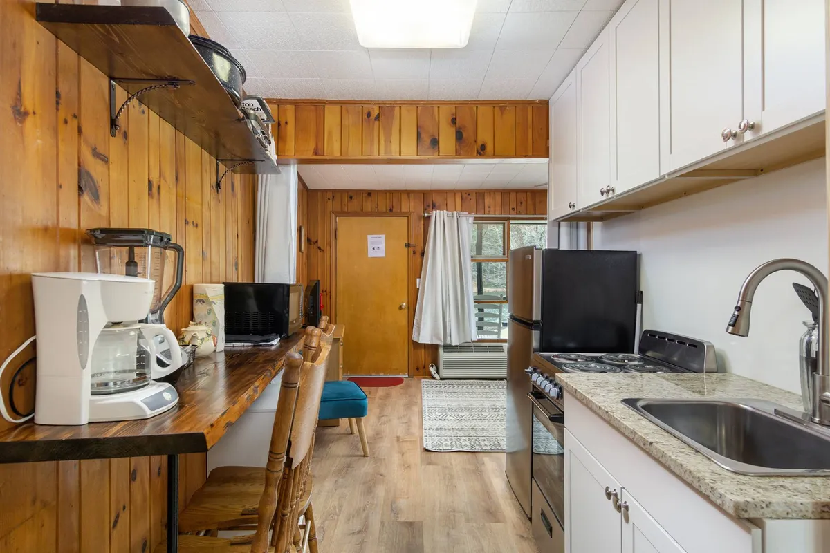 A dining area with wooden cabinetry and kitchen appliances, complemented by a set of chairs and a door leading outdoors. The scene hints at a cozy dining nook perfect for morning coffees and intimate dinners, with a glimpse of the outdoor patio beyond.