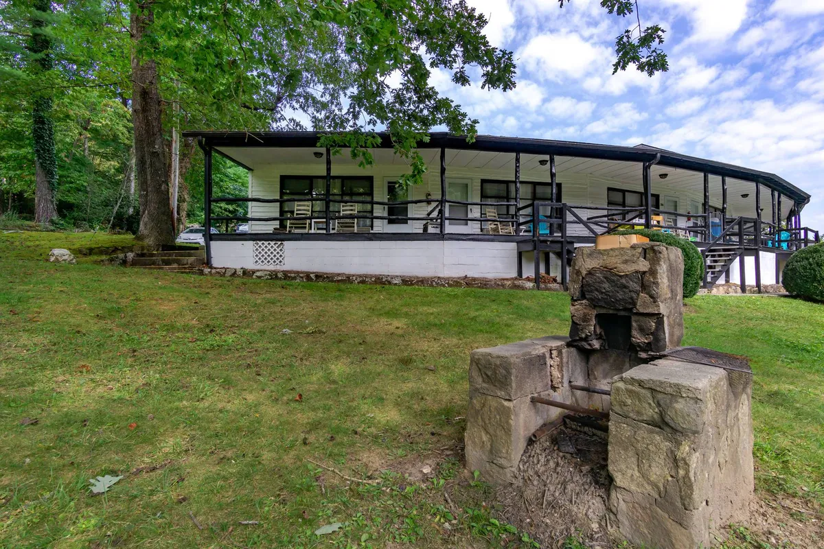 A welcoming exterior shot featuring a circular porch, a stone fire pit, and lush greenery. The scene highlights the inviting porch space, ideal for relaxing or informal gatherings, with the sunset casting a warm glow over the porch.