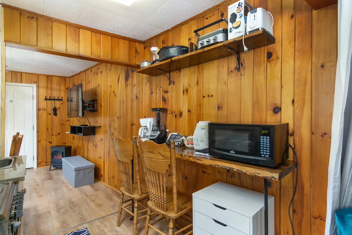 An inviting kitchen scene with wood-paneled walls, bar stools at a counter, shelves stocked with kitchen essentials, and visible kitchen appliances. The space encourages both meal preparation and casual conversation, capturing the heart of the home.