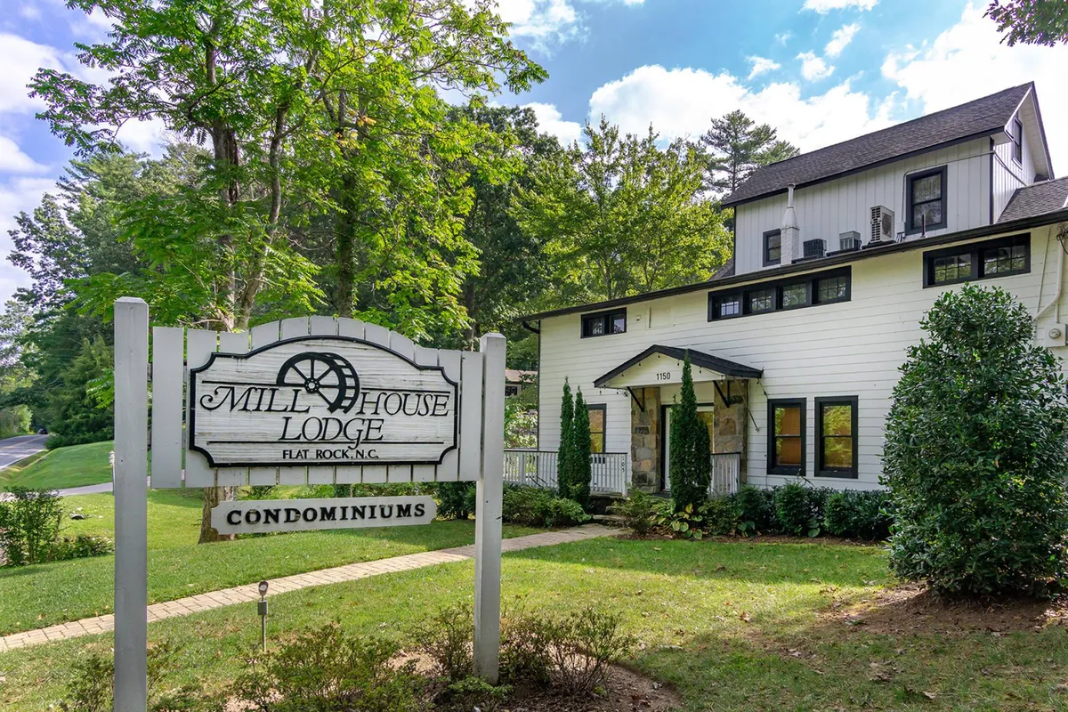 An exterior view of the Mill House Lodge sign and condominium building, surrounded by greenery and garden pathways. The scene creates a sense of welcome and community, inviting guests to explore the property and its surroundings.