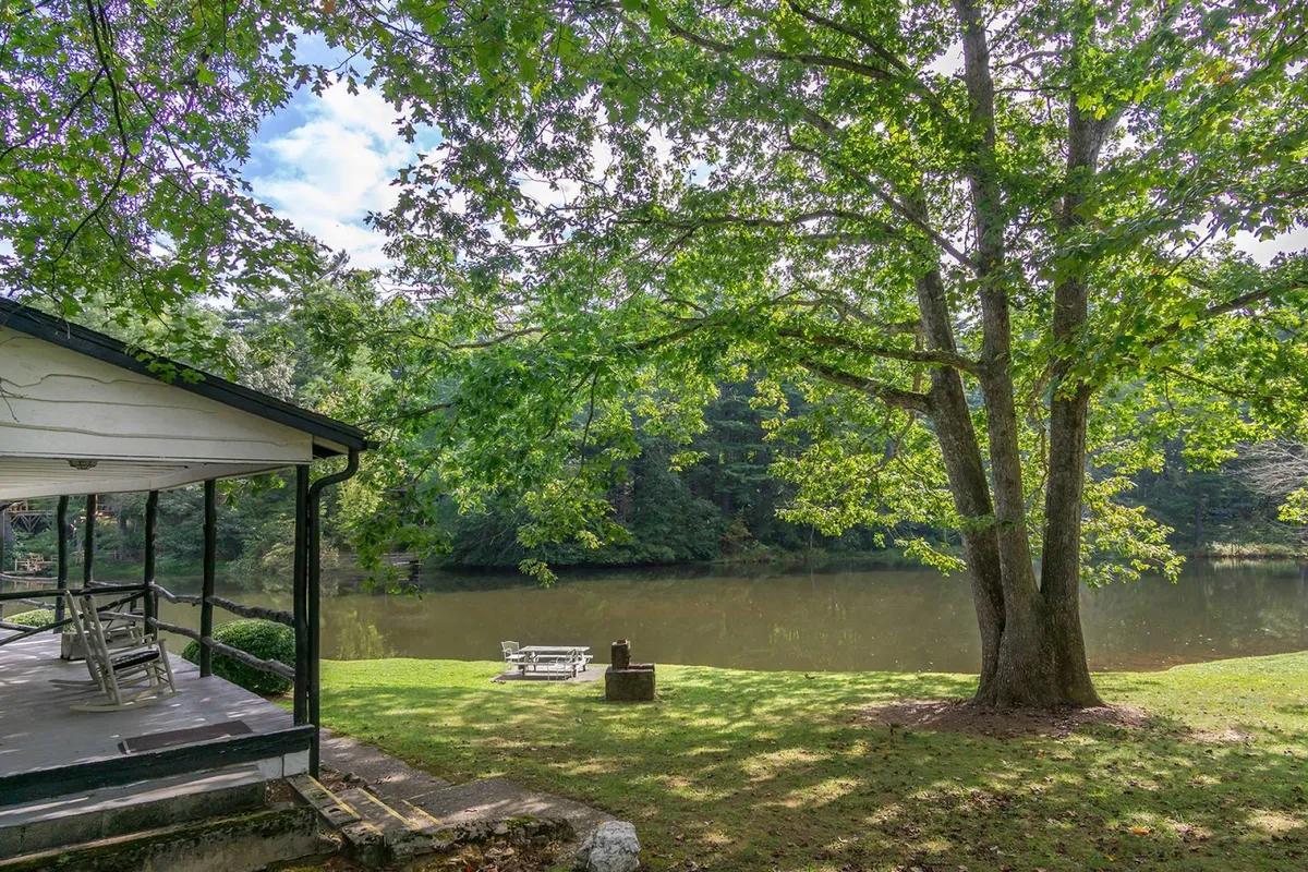 This exterior image features a serene lake bordered by lush trees, with a welcoming porch overlooking the water. The porch provides an intimate vantage point for enjoying the tranquil setting, and the gentle curve of the shoreline hints at opportunities for relaxing or sharing a quiet picnic. The overall ambiance is peaceful and intimate, ideal for couples seeking romance and relaxation.