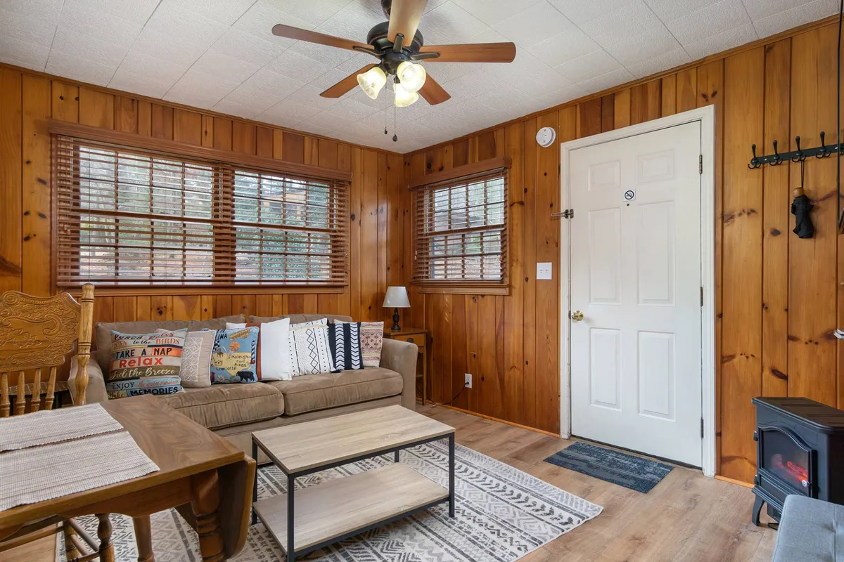 A comfortable seating area with wooden walls, a sofa adorned with decorative pillows, a coffee table, and a ceiling fan. The ambiance is tranquil and welcoming, ideal for settling in after exploring or working remotely.